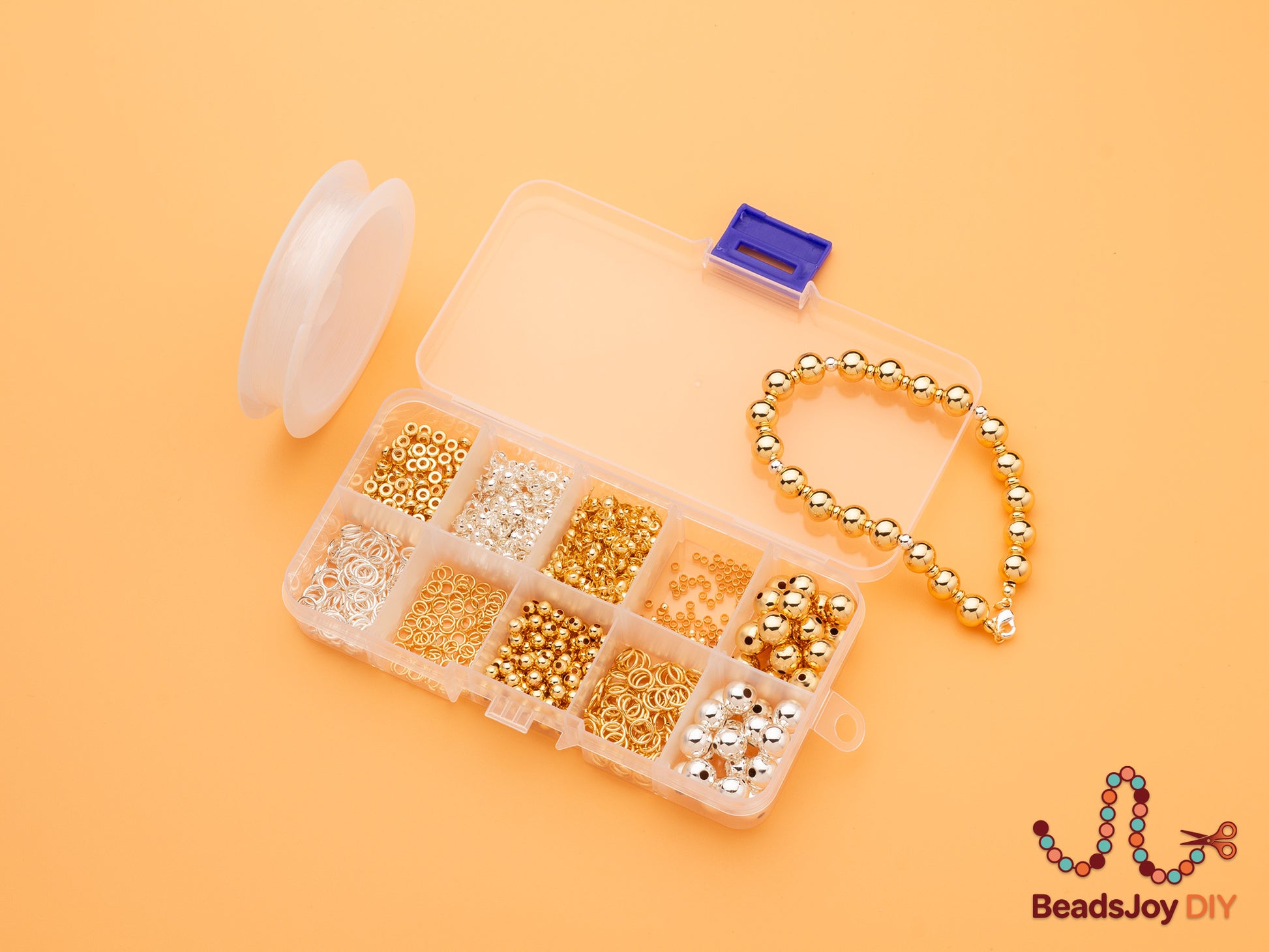 Open 10-grid clear storage box with gold and silver beads and jump rings, displayed with a completed gold bead bracelet and stretch cord on orange background