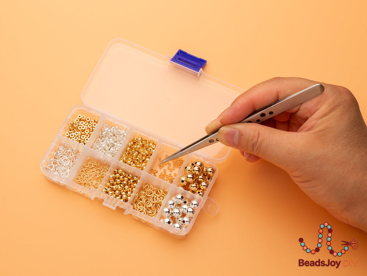 Hand using tweezers to pick beads from a 10-grid storage box filled with gold and silver beads, jump rings and findings – BeadsJoy DIY jewelry making kit