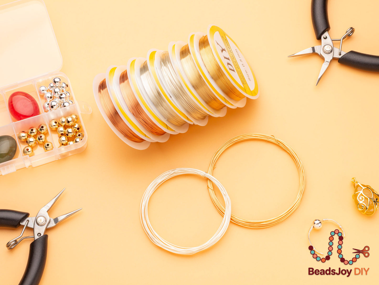 DIY jewelry wire kit flatlay with gold, silver and rose gold wire spools, pliers, beads and wire loops on orange background