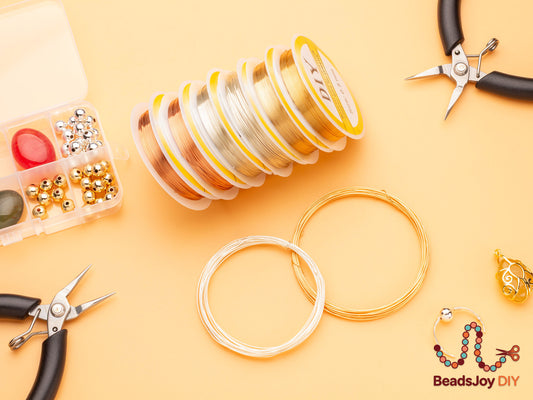 DIY jewelry wire kit flatlay with gold, silver and rose gold wire spools, pliers, beads and wire loops on orange background