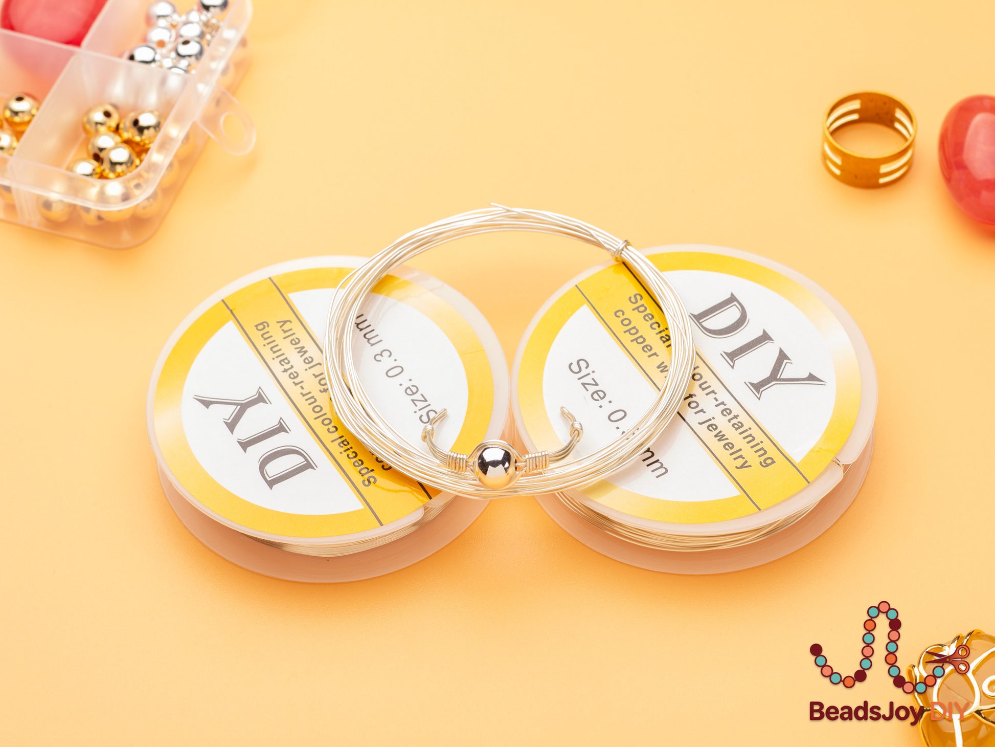 Silver colour-retaining copper wire spools 0.3mm with handmade beaded bracelet, gold ring and beads on orange background